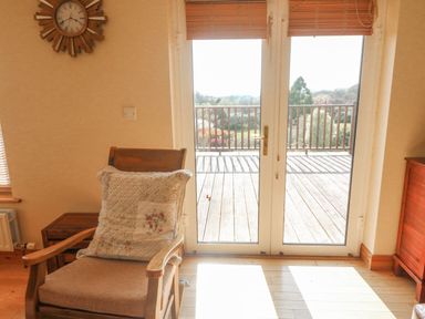 A wooden chair with a cushion facing glass doors that open to a balcony with a wooden railing at Bluebell House and Gardens in Gurteenulla near Ballydehob County Cork