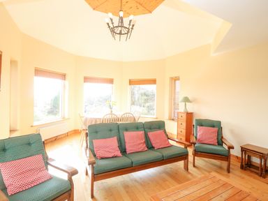 A living room with green sofas and red pillows near windows and a dining table at Bluebell House and Gardens Gurteenulla near Ballydehob County Cork