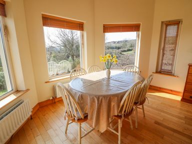 A dining area with a table covered by a tablecloth surrounded by chairs and a vase of flowers on the table at Bluebell House and Gardens in Gurteenulla near Ballydehob County Cork
