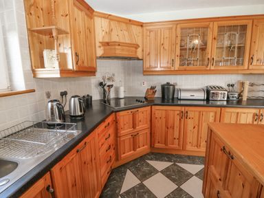 A kitchen with wooden cabinets and black countertops with a sink kettles toaster and a stove at Bluebell House and Gardens Gurteenulla near Ballydehob County Cork