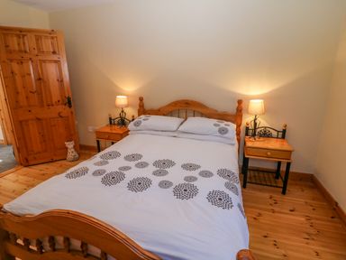 A bedroom with a wooden bed with white patterned bedding wooden side tables with lamps and a wooden door at Bluebell House and Gardens Gurteenulla near Ballydehob County Cork