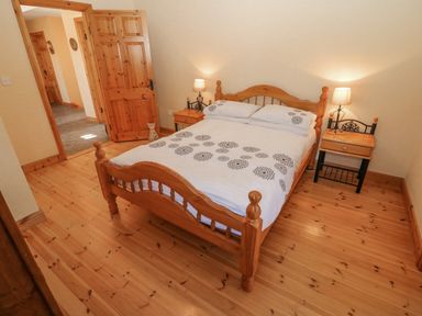 A bedroom with a wooden double bed two bedside tables with lamps and an open door at Bluebell House and Gardens Gurteenulla near Ballydehob County Cork