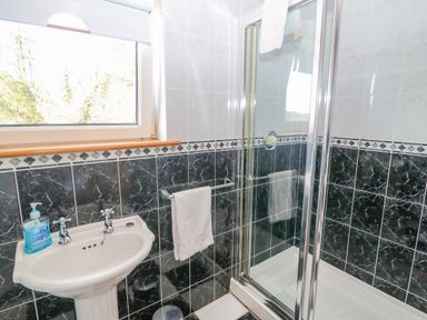A bathroom with a pedestal sink a soap dispenser a towel rack with a towel a window and a glass shower enclosure at Bluebell House and Gardens Gurteenulla near Ballydehob County Cork