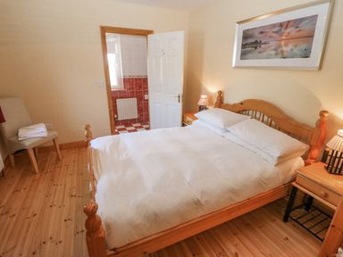 A bedroom with a wooden bed and bedside tables with lamps a chair with towels and an open door leading to a bathroom at Bluebell House and Gardens Gurteenulla near Ballydehob County Cork