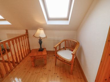 A small seating area with a wooden chair and side table with a lamp next to a wooden railing under skylight windows at Bluebell House and Gardens in Gurteenulla near Ballydehob County Cork