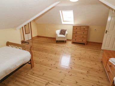 An attic bedroom with a wooden bed frame a white armchair with a cushion a chest of drawers and wooden flooring at Bluebell House and Gardens Gurteenulla near Ballydehob County Cork