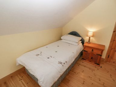 A bedroom with a single bed next to a wooden nightstand with a lamp at Bluebell House and Gardens Gurteenulla near Ballydehob County Cork