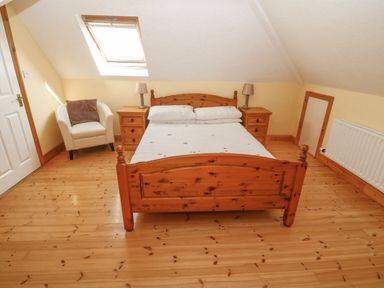 A bedroom with a wooden bed and two bedside tables with lamps and a white armchair under a skylight at Bluebell House and Gardens in Gurteenulla near Ballydehob County Cork