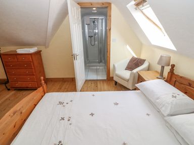 A bedroom with a wooden bed a chest of drawers a white armchair and an ensuite bathroom at Bluebell House and Gardens Gurteenulla near Ballydehob County Cork