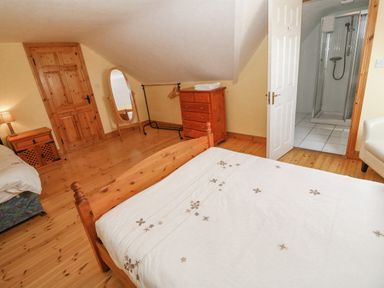 A bedroom with wooden bed and floor a dresser standing mirror and a door leading to a bathroom at Bluebell House and Gardens Gurteenulla near Ballydehob County Cork