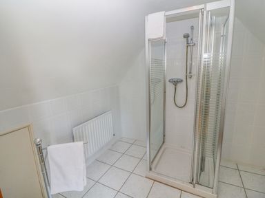 A tiled bathroom with a glass shower enclosure a white towel on a metal rail and a radiator on the wall at Bluebell House and Gardens Gurteenulla near Ballydehob County Cork