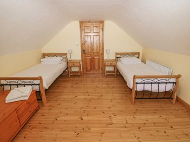 A bedroom with two single beds two bedside tables with lamps a wooden door and a wooden chest of drawers at Bluebell House and Gardens Gurteenulla near Ballydehob County Cork