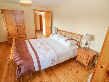 A bedroom with a wooden bed frame bedside table with lamp and wooden wardrobe at Bluebell House and Gardens Gurteenulla near Ballydehob County Cork