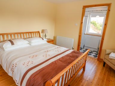 A bedroom with a wooden bed and bedside table next to a doorway showing a bathroom at Bluebell House and Gardens in Gurteenulla near Ballydehob County Cork