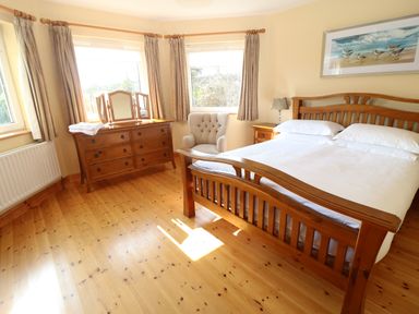 A bedroom with a wooden bed, dresser, armchair, and nightstand at Bluebell House and Gardens in Gurteenulla near Ballydehob County Cork