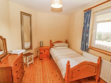 A bedroom with a single bed bedside table dresser stool wall mirror and window at Bluebell House and Gardens Gurteenulla near Ballydehob County Cork