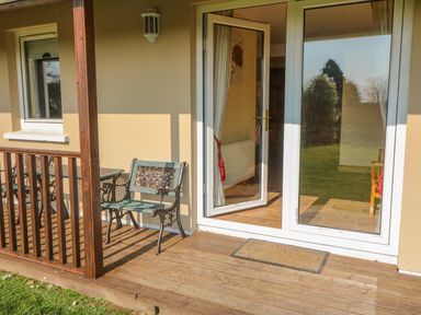 A wooden deck with metal chair and table outside a glass door at Bluebell House and Gardens Gurteenulla near Ballydehob County Cork