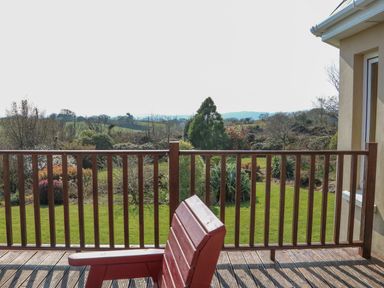A wooden deck with a red chair overlooking a garden and distant fields at Bluebell House and Gardens in Gurteenulla near Ballydehob County Cork