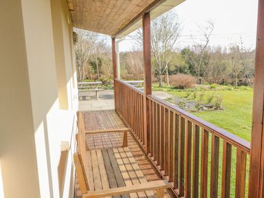 A wooden bench on a covered porch with a view of a garden at Bluebell House and Gardens Gurteenulla near Ballydehob County Cork