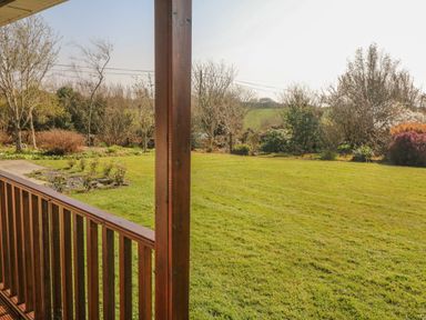 A wooden porch overlooking a grassy garden with various shrubs and trees at Bluebell House and Gardens in Gurteenulla near Ballydehob County Cork