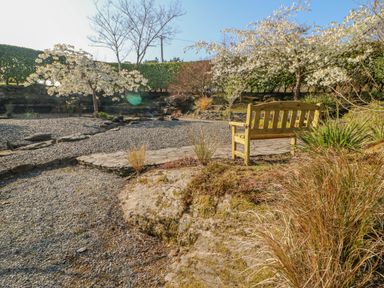 A wooden bench on a stone patio in a garden with gravel paths and flowering trees at Bluebell House and Gardens Gurteenulla near Ballydehob County Cork
