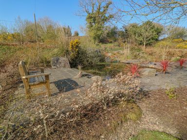 A wooden bench beside a small pond surrounded by stone paving and plants at Bluebell House and Gardens in Gurteenulla near Ballydehob County Cork