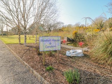 An outdoor garden area with a sign reading Bluebell House and Gardens near a gravel path and trees at Bluebell House and Gardens Gurteenulla near Ballydehob County Cork