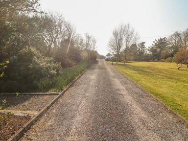 A gravel driveway with a parked car at the end surrounded by grass and trees at Bluebell House and Gardens Gurteenulla near Ballydehob County Cork