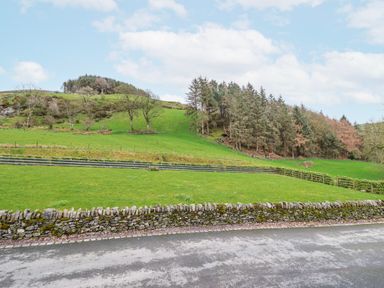 A view of a grassy hill with trees and a stone wall at Briws and 963354 together they sleep 35