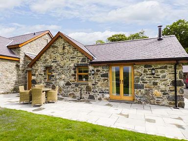 Stone house with wooden door and windows a patio with table and chairs and a lawn at Beudy in Llangwm near Bala