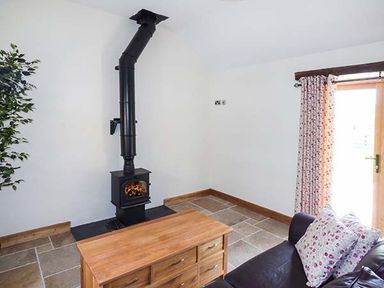 A living room with a black wood stove chimney a wooden table a dark sofa with floral cushions and a door with floral curtains at Beudy in Llangwm near Bala