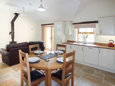 A kitchen and dining area with a round wooden table set for four and a sofa in the background at Beudy in Llangwm near Bala
