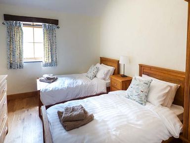 A bedroom with two single beds a bedside table with a lamp and a window with patterned curtains at Beudy in Llangwm near Bala