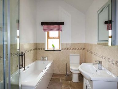 A bathroom with a bathtub toilet sink and a small window with a red and white curtain at Beudy in Llangwm near Bala