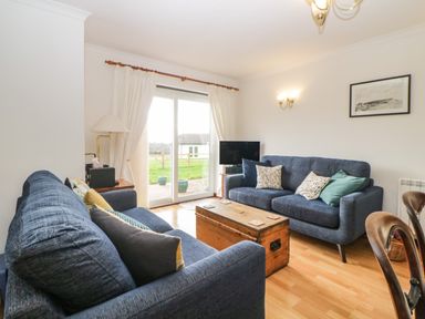 A living room with two blue sofas a wooden chest as a coffee table and a tv near a sliding glass door at Broom Cottage Stoneleigh Holiday Village near Sidmouth