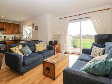 A living room with two blue sofas and wooden chest table near sliding glass doors at Broom Cottage in Stoneleigh Holiday Village near Sidmouth