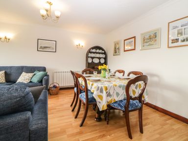 A dining area with a table set for six and a blue sofa with cushions in a living room at Broom Cottage Stoneleigh Holiday Village near Sidmouth