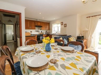 A dining table with plates and glassware next to a kitchen and living area with sofa at Broom Cottage Stoneleigh Holiday Village near Sidmouth
