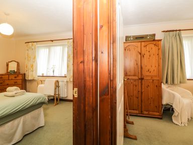 Two adjoining rooms with wooden furniture a bed and a chair in one room and a wardrobe and an armchair in the other at Broom Cottage in Stoneleigh Holiday Village near Sidmouth