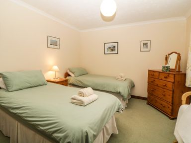 A bedroom with two single beds green bedding a wooden dresser with mirror and a bedside table with lamp at Broom Cottage Stoneleigh Holiday Village near Sidmouth
