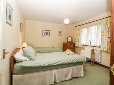 A bedroom with two single beds a wooden dresser and floral curtains at Broom Cottage Stoneleigh Holiday Village near Sidmouth