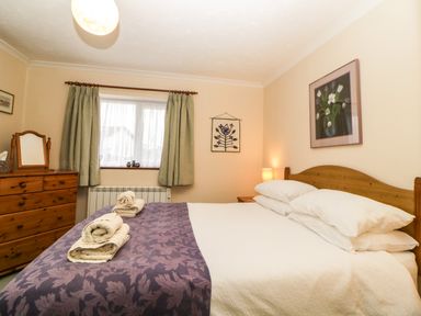 A bedroom with a wooden bed and dresser with towels on the bed at Broom Cottage Stoneleigh Holiday Village near Sidmouth