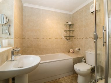 A bathroom with a sink, bathtub, toilet, glass shower enclosure, and tiled walls at Broom Cottage Stoneleigh Holiday Village near Sidmouth
