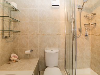A bathroom with a toilet shower enclosure glass shelves seashells and tiled walls at Broom Cottage Stoneleigh Holiday Village near Sidmouth