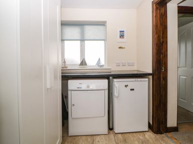A utility room with a washing machine and a small refrigerator under a countertop at Broom Cottage Stoneleigh Holiday Village near Sidmouth