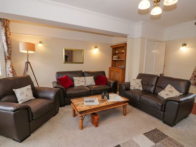 A living room with three brown leather sofas a wooden coffee table a floor lamp and a wooden cabinet at The Farm House in Bala