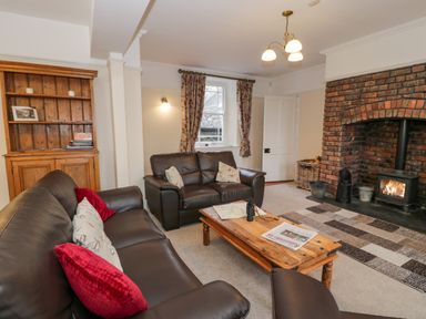 A living room with brown leather sofas a wooden coffee table a brick fireplace with a wood stove and a wooden cabinet at The Farm House in Bala