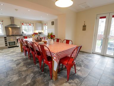 A kitchen with a large dining table covered with a red and white checkered tablecloth and red chairs at The Farm House in Bala