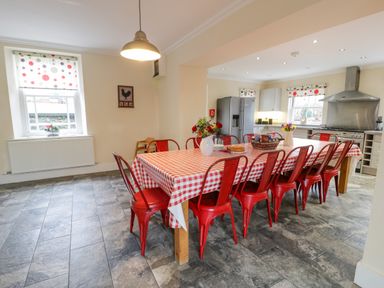 A kitchen with a large dining table with red metal chairs and a checkered tablecloth at The Farm House in Bala