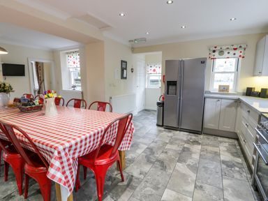 A kitchen with a red and white checkered tablecloth on a dining table surrounded by red chairs and a stainless steel refrigerator at The Farm House in Bala